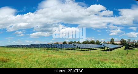 Solarkraftwerk im Herbst. Sonnenkollektoren auf orangefarbenem Grasfeld unter blauem Himmel mit Wolken Stockfoto