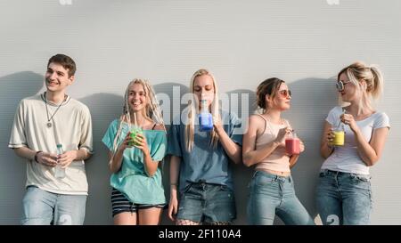 Gruppe von jungen modernen Menschen trinken bunte Smoothies Getränke und reden, lehnte sich an der Wand Stockfoto