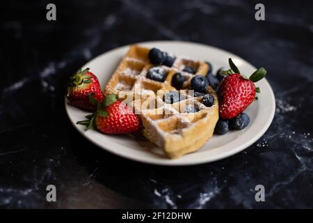 Waffeln, Erdbeeren und Heidelbeeren auf einer Granittheke Stockfoto