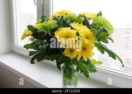 Bouquet von gelben Chrysanthemen und Grün steht auf der Fensterbank Stockfoto