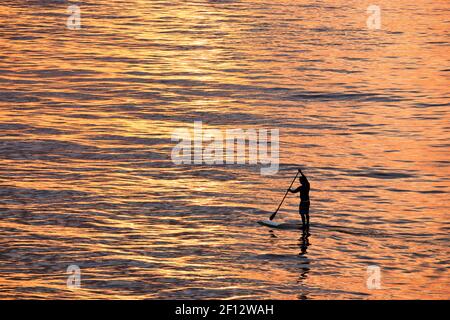 Mann paddeln im orangefarbenen Sonnenuntergang Wasser Stockfoto