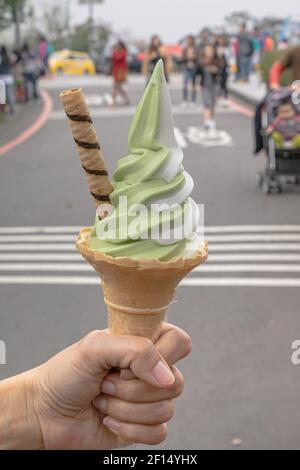 Eis-Kegel, eine Nahaufnahme von Matcha grünem Tee und Vanille weich serviert mit Waffel-Kegel in der Hand halten auf Reise Straße mit Menschen Hintergrund in Tai Stockfoto