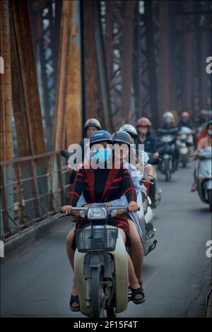 Vietnamesische Stadtpendler auf Motorrädern über die historische lange Bien-Brücke, Hanoi, Vietnam. Zwei Frauen reiten Pillion Stockfoto