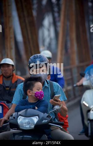 Vietnamesische Stadtpendler auf Motorrädern über die historische lange Bien-Brücke, Hanoi, Vietnam. Vatermit Telefon, und Sohn. Stockfoto