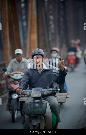 Vietnamesische Stadtpendler auf Motorrädern über die historische lange Bien-Brücke, Hanoi, Vietnam. Friedenszeichen. Stockfoto