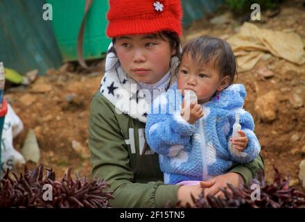 Junge vietnamesische Mutter mit ihrem kleinen Kind. Verkauf von roten getrockneten Chilischoten auf Can CAU Markt, Vietnam, Lao Cai Provinz, Vietnam Stockfoto