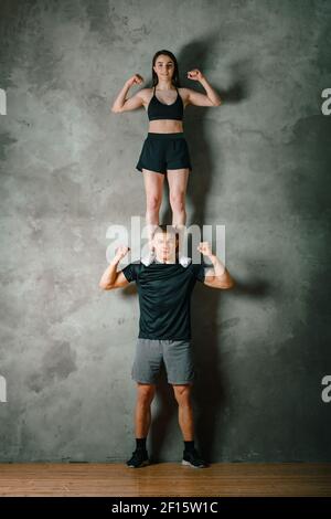 Ein Mann und eine Frau Athleten stehen auf einem grauen Hintergrund übereinander. Gymnastik Workouts, Akrobaten Heimtricks Stockfoto