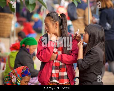 Junge Blumen Hmong Frauen in moderner Kleidung. Eines mit Mobiltelefon. BAC Ha Markt, Lao Cai Provinz, Vietnam Stockfoto