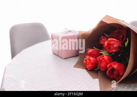 Ein Bouquet aus roten Tulpen auf dem Tisch und rosa Geschenkbox. Konzept für eine Grußkarte. Hochwertige Fotos Stockfoto