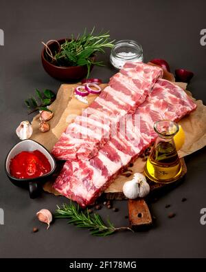 Frische rohe Schweinefleischrippen gewürzt mit Gewürzen auf dunklem Hintergrund. Stockfoto
