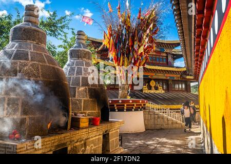 Guishan Dafo Tempel Blick mit dampfenden Opfer Brennen und Gebet Flaggen Dharma Rad im Hintergrund in Dukezong Altstadt in Shangri-La Yunnan China Stockfoto