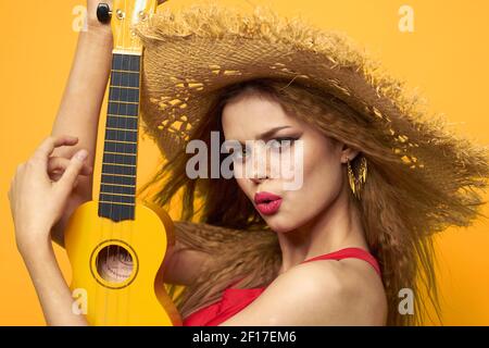 Frau in rot hat Ukulele in den Händen Lifestyle Sommer rot t-Shirt gelb Hintergrund Stockfoto