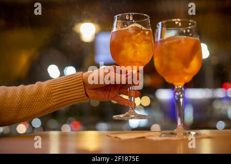Nahaufnahme der Frau Hände halten Glas mit Cocktail von oranger Farbe. Ein weiteres Glas steht auf dem Tisch. Stockfoto