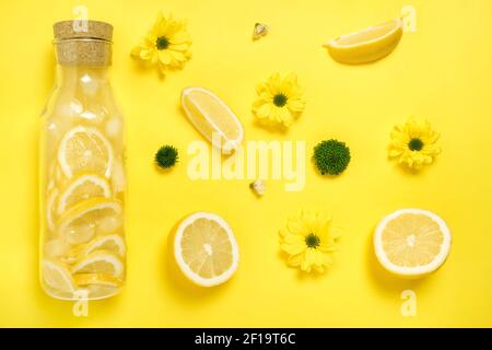 Flach Lay Lemonade in Glasflasche mit Zitronen, Blumen gelb Papier Hintergrund Stockfoto