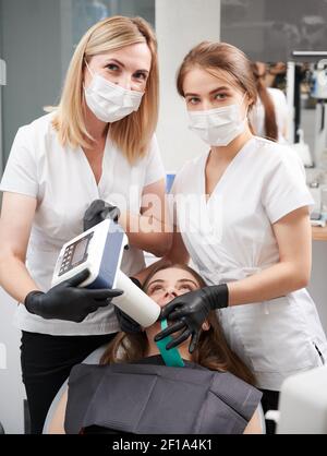 Ärzte mit tragbaren zahnmedizinischen Röntgengerät bei der Untersuchung weiblichen Patienten Zähne in der Zahnarztpraxis. Junge Frau liegt im Stuhl, während Zahnärzte Durchführung intraoralen Scanning mit modernen Geräten. Stockfoto