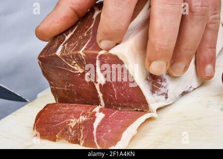 Trocken gehärteter Schinken in dünne Scheiben geschnitten Closeup auf Chef Hände Scheiben Prosciutto Italienische Delikatessen Stockfoto