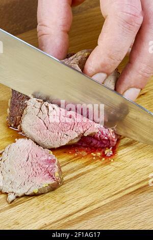 Der Koch schneidet gegrilltes Fleisch auf dem Brett mit einem vollen Serie von Blut Rezept Kochen Stockfoto