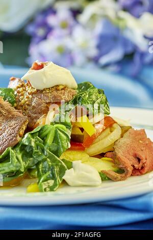 Fleischsalat mit grünen Tomaten auf dem Teller blauer Hintergrund Viele Rezepte für Lebensmittel Stockfoto