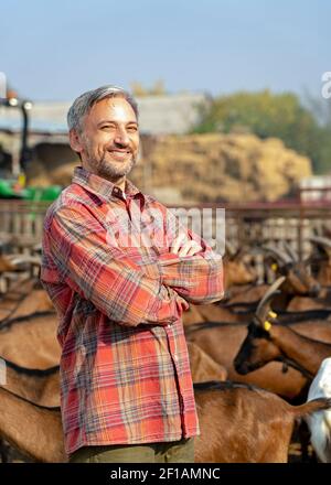 Lächelnder reifer Bauer steht in einem Outdoor-Tiergehege in ländlicher Landschaft. Konzept Der Tierhaltung. Stockfoto