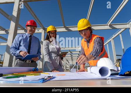 Ingenieur, Architekt und lächelnder Geschäftsmann beim Überprüfen des Bauprints auf der Baustelle. Geschäftsbeziehung und Teamwork-Konzept. Stockfoto