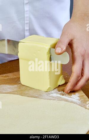 Der Koch schneidet ein großes Stück Butter auf dem Teig Vorbereitung Käsekuchen Serie voll Kochen Lebensmittel Rezepte Stockfoto