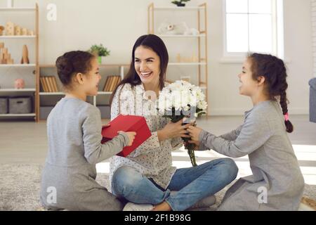 Glücklich lächelnde Frau Mutter sitzt auf dem Boden zwischen ihren Töchtern Und Blumen und Geschenke bekommen Stockfoto