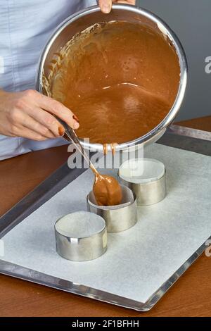 Der Koch gießt den Teig in Formen für die Herstellung von Cupcakes Stockfoto