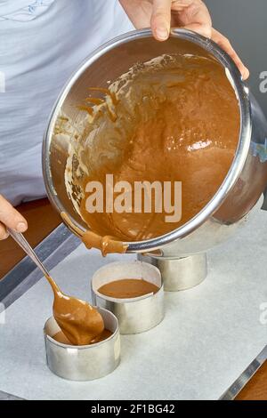 Der Koch gießt den Teig in Formen für die Herstellung von Cupcakes Stockfoto