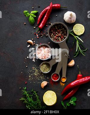 Vielfalt an bunten Gewürzen in Löffeln. Salzflocken, gemischter Pfeffer, Rosmarin, Basilikum und Knoblauch auf dunkelschwarzem Schiefergrund. Draufsicht. Speicherplatz kopieren. Stockfoto