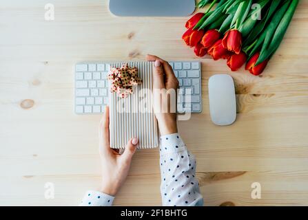 Draufsicht auf weibliche elegante Hände halten Geschenkverpackung Box über Computer-Tastatur am Arbeitsplatz im Büro. Lieferung von Geschenken und Internet-Bestellungen. Stockfoto