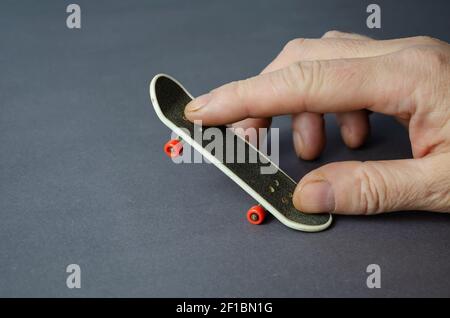 Mini Skate und Hand auf grauem Hintergrund. Männliche Hand spielt Finger Skateboard. Nahaufnahme, selektiver Fokus. Stockfoto