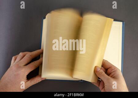 Verschwommene Bewegung der Hand Umdrehen Seite über grauen Hintergrund. Männliche Hände blättern schnell durch ein altes Buch mit vergilbten Seiten. Mann mittleren Alters, kaukasisch. Stockfoto