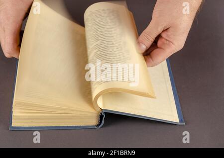 Verschwommene Bewegung der Hand Umdrehen Seite über grauen Hintergrund. Männliche Hände blättern schnell durch ein altes Buch mit vergilbten Seiten. Mann mittleren Alters, kaukasisch. Stockfoto