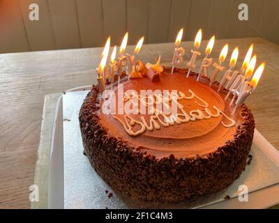Hausgemachte Schokolade Geburtstagstorte mit brennenden Kerzen auf einem Küchentisch Aus Wiedergewonnener Eiche Stockfoto