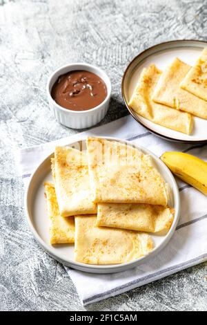 Crepes, dünne Pfannkuchen auf einem Teller. Schokoladen-Haselnuss-Aufstrich und mit Bananen gefüllte Crepes auf dem Teller. Leckere Crepes oder Blini mit süßer Sauce. Stockfoto