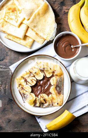 Crepes, dünne Pfannkuchen auf einem Teller. Schokoladen-Haselnuss-Aufstrich und mit Bananen gefüllte Crepes auf dem Teller. Leckere Crepes oder Blini mit süßer Sauce. Stockfoto