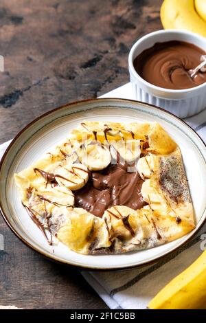 Crepes, dünne Pfannkuchen auf einem Teller. Schokoladen-Haselnuss-Aufstrich und mit Bananen gefüllte Crepes auf dem Teller. Leckere Crepes oder Blini mit süßer Sauce. Stockfoto