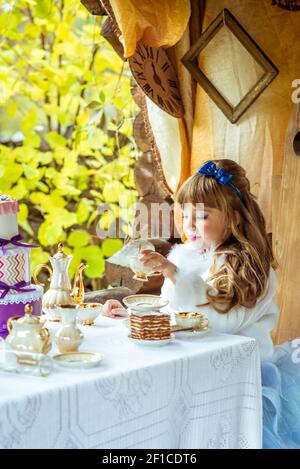 Vorderansicht eines kleinen schönen Mädchen in der Landschaft Von Alice im Wunderland mit einer Tasse Tee Die Tabelle Stockfoto