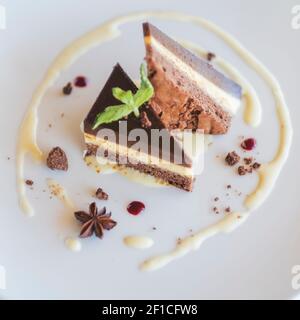 Essen und Trinken, Schokoladenkäsekuchen auf einem weißen Teller mit Anis und Sahne serviert, moderne minimalistische Optik, kein Besteck, wunderschön präsentiert Stockfoto