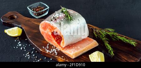 Frisches, rohes Lachssteak mit Zitrone, Herden und Gewürzen auf Schneidebrett. Stockfoto