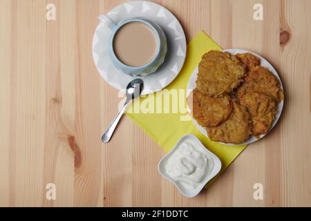 Kartoffelpfannkuchen auf einem Teller und eine Tasse Kaffee Auf einem hölzernen Hintergrund Stockfoto