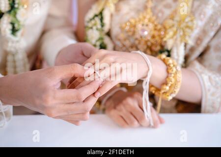 Der Bräutigam trägt einen Ehering und trägt einen Ehering am Finger der Braut. Ehering-Austausch in Thailand. Stockfoto