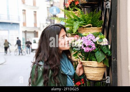 Spanisch attraktiv hübsch mittleren Alters Brünette Frau riecht Blumen aus Ein Blumenhändler auf der Straße Stockfoto
