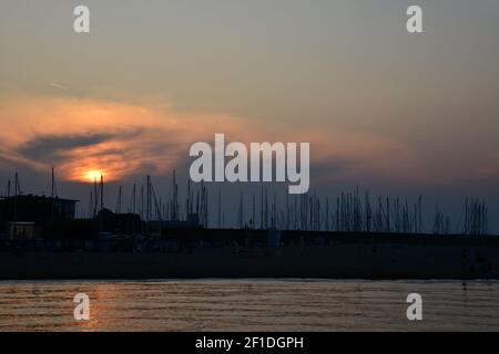 Romantischer Sonnenuntergang über dem Hafen. Rot-goldener Sonnenuntergang im Hintergrund mit Masten von Yachten und Segelbooten. Sonnenuntergang am italienischen Strand. Dunkle Meeresmasten i Stockfoto