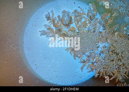 Eiskristalle bilden sich auf einer Glasplatte. Eisblumen auf einem gelben Lichtkreis. Frost auf dem Glas. Abstrakter Hintergrund mit strahlender Sonne, winziges Wasser d Stockfoto