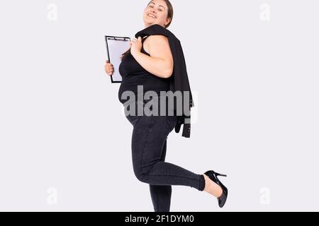 Kaukasische plump Frau im Büro tragen mit Jacke auf der Schulter und Ordner in Händen lächelnd und posiert auf isolierten weißen Hintergrund mit Seitenraum. Stockfoto