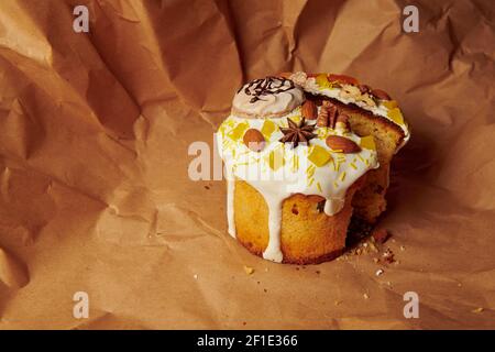 Geschnittener Osterkuchen auf braunem Papier. Handgemachte Panettone mit flüssigen Puderzucker Mandeln, Walnuss und Baiser verziert. Stockfoto