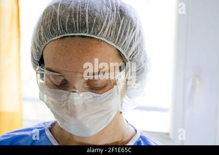 Ein flacher Fokus einer jungen Ärztin mit Schutzfunktion Brille und Gesichtsmask im Krankenhaus Stockfoto