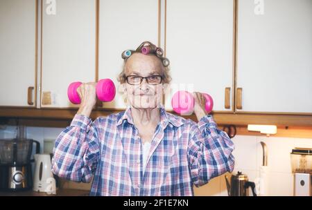 Lächelnd fröhlich ältere schwedische Frau mit rosa Hanteln in der Küche. Konzept des aktiven Lebensstils, Fitness, Gesundheit Stockfoto