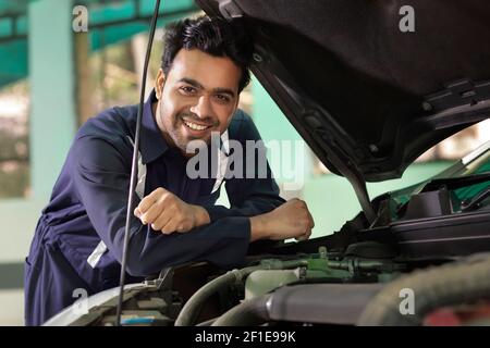 Ein männlicher Mechaniker arbeitet unter einer Motorhaube eines Auto in einer Garage Werkstatt Stockfoto